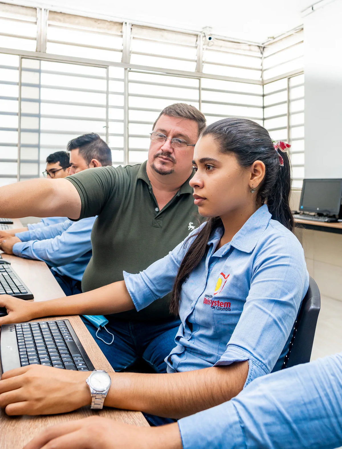 Docente y estudiante de Unisystem trabajan frente a un computador.