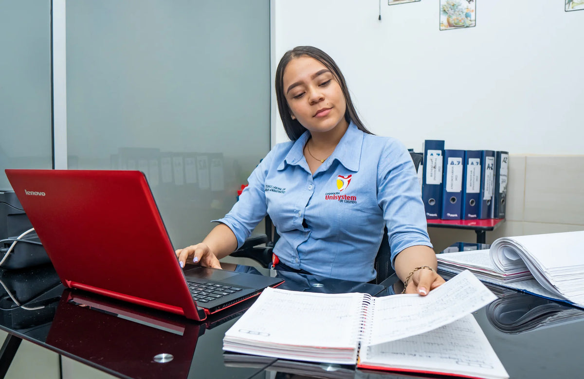 Estudiante de Unisystem consulta documentos junto a un computador y archivadores.